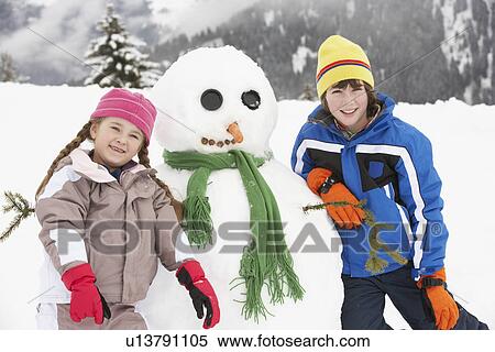 Stock Photography - Two Young Children Building Snowman On Ski Holiday In Mountains. Fotosearch