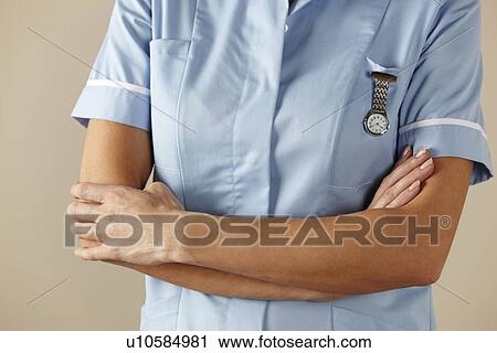 Stock Image - UK nurse standing with arms folded. Fotosearch