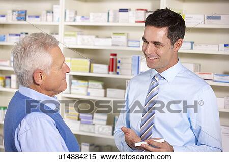 Stock Photography - UK pharmacist serving senior man in pharmacy. Fotosearch