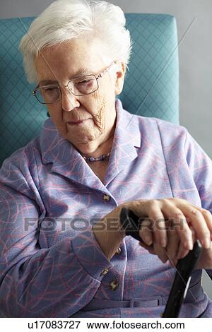 Stock Photo - Unhappy Senior Woman Sitting In Chair Holding Walking Stick. Fotosearch