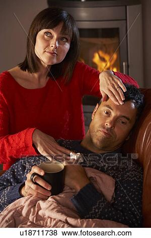 Wife Nursing Sick Husband With Cold Resting On Sofa By Cosy Log Fire View Large Photo Image Stock Photo - Wife Nursing Sick Husband With Cold Resting On Sofa By Cosy Log Fire. Fotosearch