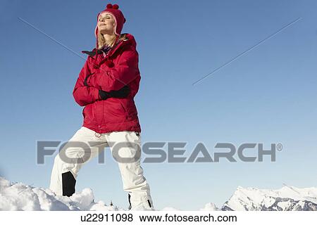 Stock Photo - Woman Standing In Snow Wearing Warm Clothes On Ski Holiday In Mountains. Fotosearch