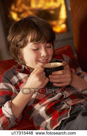 Stock Photo - Young Boy Relaxing With Hot Drink By Cosy Log Fire. Fotosearch