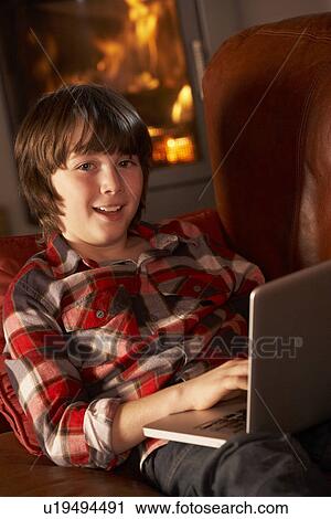 Stock Image - Young Boy Relaxing With Laptop By Cosy Log Fire. Fotosearch