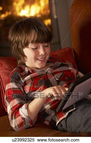 Stock Photography - Young Boy Relaxing With Tablet Computer By Cosy Log Fire. Fotosearch