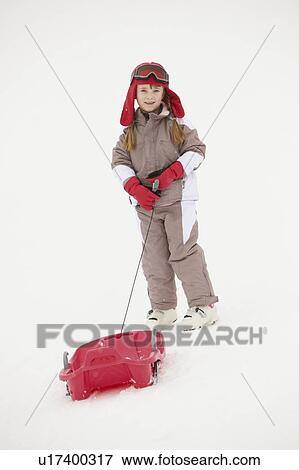 Stock Photo - Young Girl Pulling Sledge On Ski Holiday In Mountains. Fotosearch
