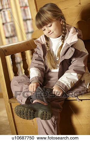 Stock Image - Young Girl Sitting On Wooden Seat Putting On Warm Outdoor Clothes And Boots. Fotosearch
