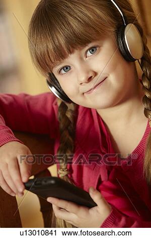Stock Image - Young Girl Sitting On Wooden Seat Listening To MP3 Player. Fotosearch