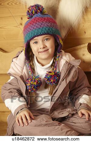 Stock Image - Young Girl Sitting On Wooden Seat Wearing Warm Outdoor Clothes. Fotosearch