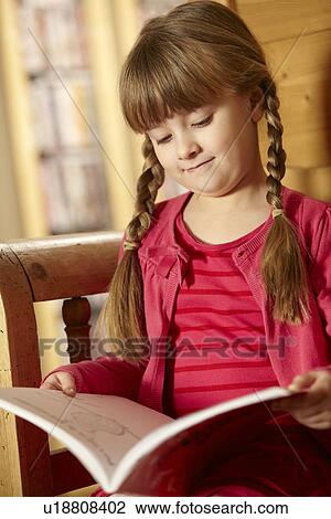Stock Image - Young Girl Sitting On Wooden Seat Reading Book. Fotosearch
