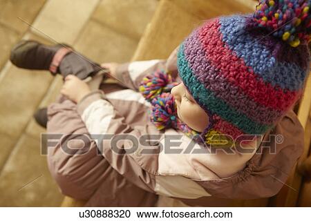 Stock Image - Young Girl Sitting On Wooden Seat Putting On Warm Outdoor Clothes And Boots. Fotosearch