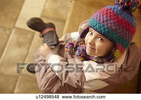 Stock Photo - Young Girl Sitting On Wooden Seat Putting On Warm Outdoor Clothes And Boots. Fotosearch