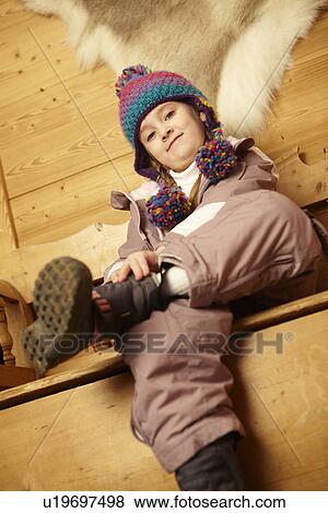 Stock Photo - Young Girl Sitting On Wooden Seat Putting On Warm Outdoor Clothes And Boots. Fotosearch