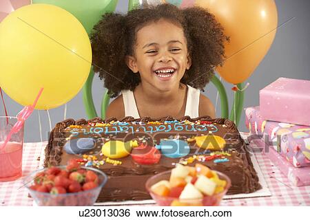 Stock Photograph - Young girl with birthday cake and gifts at party. Fotosearch
