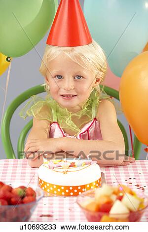 Stock Image - Young girl with birthday cake at party. Fotosearch