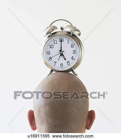 Stock Photography - Back view of man with alarm clock on shaved head. Fotosearch