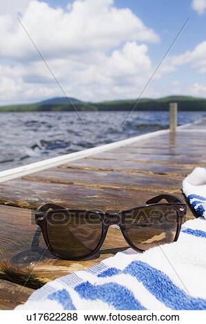 Stock Photo - Close-up of sunglasses and towel on jetty. Fotosearch