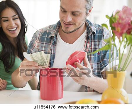 Couple putting money in savings jar View Large Photo Image Stock Photograph - Couple putting money in savings jar. Fotosearch