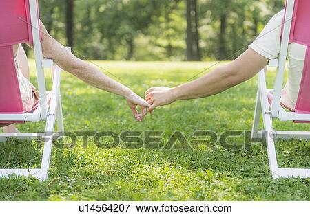 Stock Photo - Couple sitting on deck chairs and holding hands. Fotosearch