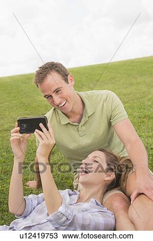 Stock Image - Couple sitting on lawn with camera. Fotosearch