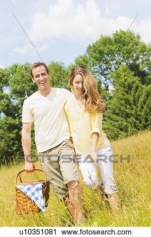 Stock Image - Couple walking with picnic basket on meadow. Fotosearch