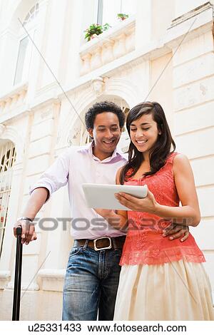 Stock Image - France, Cassis, Couple using digital tablet on street. Fotosearch