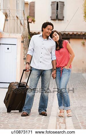 Stock Image - France, Cassis, Couple with suitcase holding hands. Fotosearch