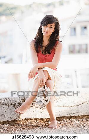 Stock Image - France, Cassis, Young woman sitting on stone wall. Fotosearch