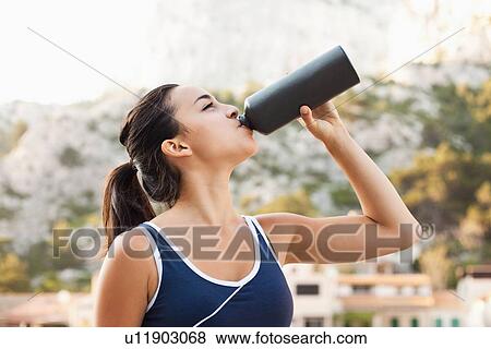Stock Photo - France, Marseille, Young woman in tracksuit drinking water. Fotosearch