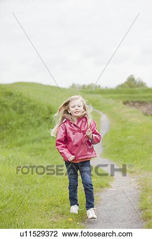 Stock Image - Girl in pink raincoat on country path. Fotosearch