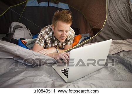 Stock Image - Hiker in tent using laptop. Fotosearch