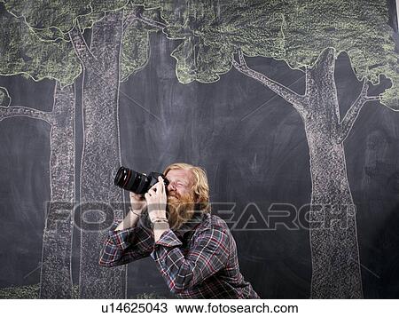 Stock Image - Man in front of blackboard taking pictures. Fotosearch