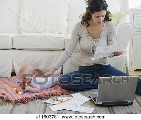 Stock Image - Mother with baby boy (2-5 months) sorting home finances. Fotosearch