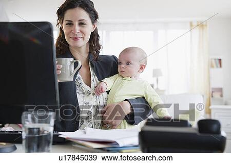 Stock Photo - Mother with baby boy (2-5 months) working from home. Fotosearch