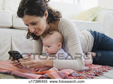 Stock Photography - Mother with baby boy (2-5 months) text messaging. Fotosearch