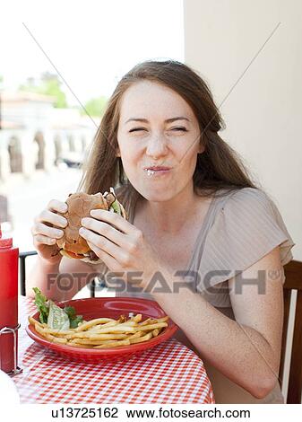 Stock Image - Portrait of young woman having burger. Fotosearch