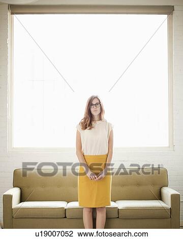 Portrait of young woman standing in front of sofa View Large Photo Image Stock Image - Portrait of young woman standing in front of sofa. Fotosearch