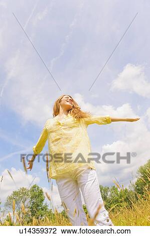 Stock Image - Portrait of young woman standing on meadow. Fotosearch