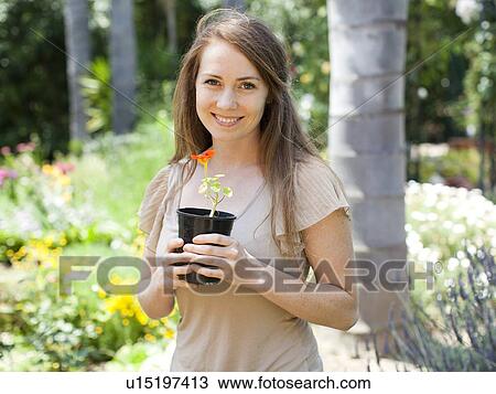 Stock Image - Portrait of young woman with flower in pot. Fotosearch