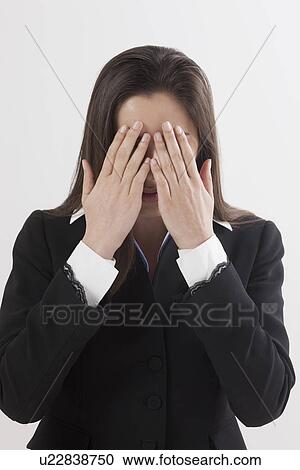 Stock Image - Portrait of young woman with hands covering eyes, studio shot. Fotosearch