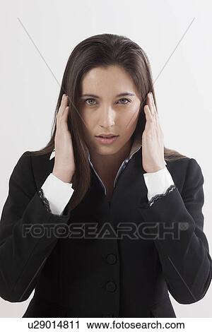Stock Image - Portrait of young woman with hands covering ears, studio shot. Fotosearch