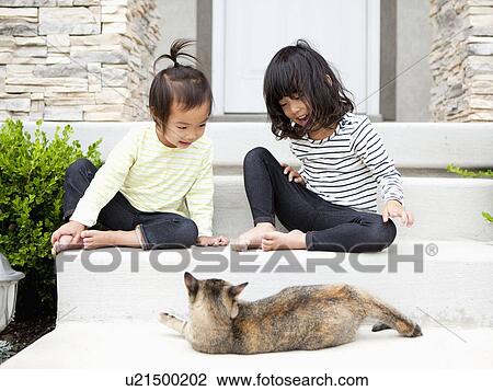Stock Image - Sisters (2-3, 4-5) sitting in front of house with cat. Fotosearch