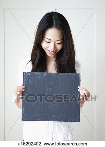 Stock Image - Smiling young woman holding blackboard, studio shot. Fotosearch