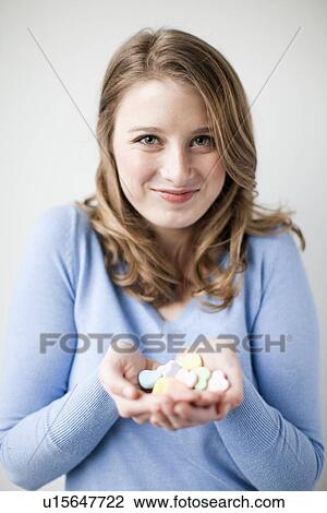 Stock Image - Studio shot of smiling woman holding heart-shaped sweets. Fotosearch