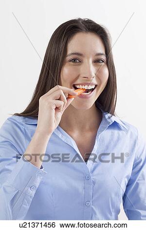 Stock Photograph - Studio shot of woman eating baby carrots. Fotosearch