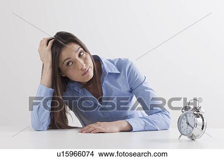 Picture - Studio shot of woman waiting by alarm clock. Fotosearch
