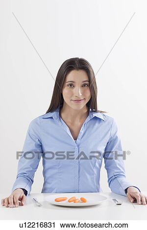 Stock Image - Studio shot of woman with baby carrots on plate. Fotosearch