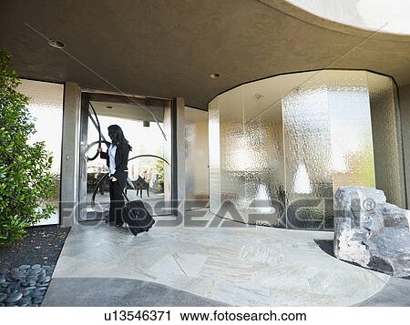 Stock Image - Woman leaving house with piece of luggage. Fotosearch
