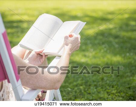 Stock Image - Woman sitting on deck chair and reading book. Fotosearch