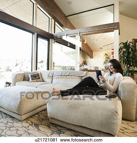 Stock Image - Woman using tablet while sitting on couch. Fotosearch